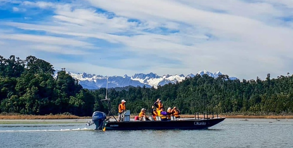 Travellers on a nature cruise on Okarito Lagoon with the Southern Alps in the background, West Coast, South Island, New Zealand.